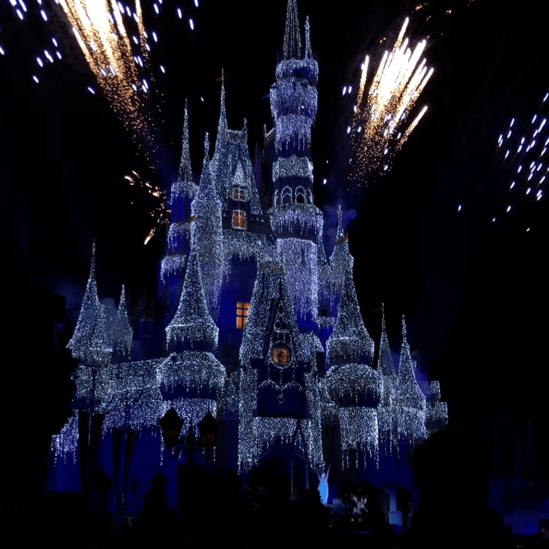 Cinderella's castle covered in white Christmas lights and fireworks going off.