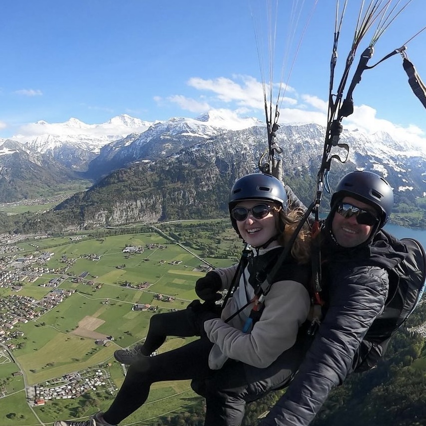 Blonde woman and male instructor paragliding over Interlaken, Switzerland. Mountains, valley, lake all behind them