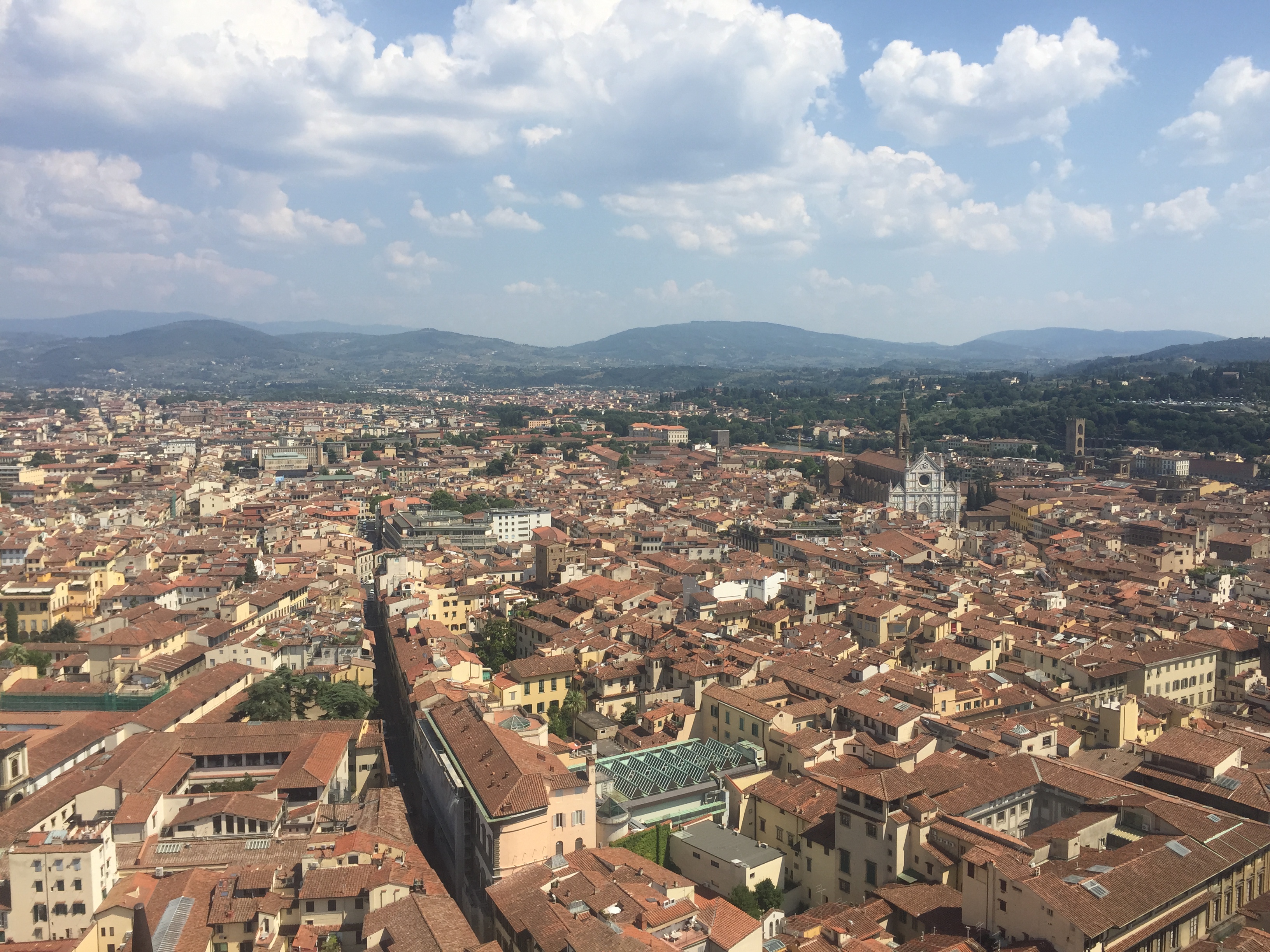 View of Florence, Italy from higher ground. Tops of buildings, churches, and mountains in the distance.